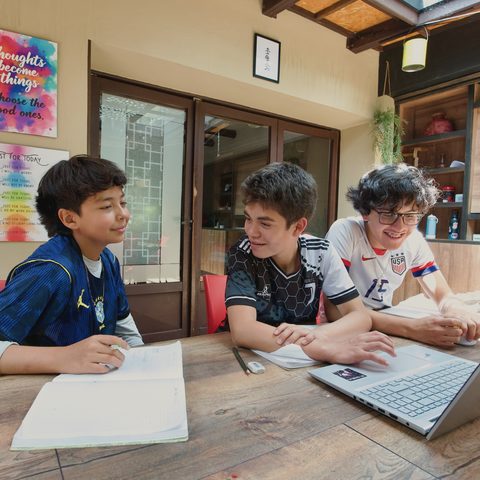 Tres jóvenes sonríen mientras trabajan con un portátil y sus cuadernos